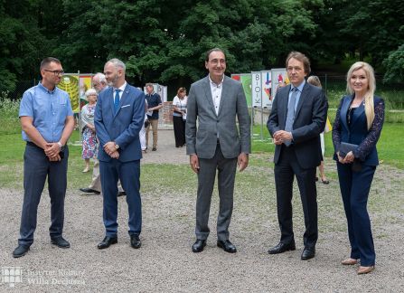 fotografia. art piknik w willi decjusza. pięć elegancko ubranych osób stoi, jedna obok drugiej, na żwirowym placu przed willą.